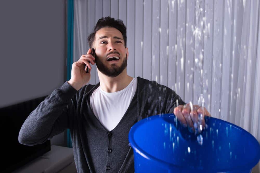 When to Call an Emergency Plumbing Service A man on the phone with a bucket of water.