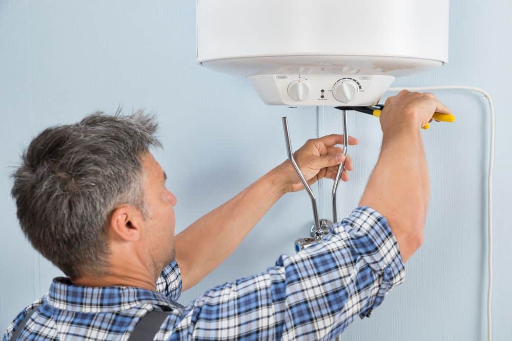 Have a Water Heater Leak? Here’s What to Do A man working on the top of a water heater.